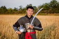 Portrait of a medieval warrior in armor with a weapon in his hands against the background of a wheat field and sky