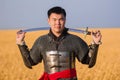 Portrait of a medieval warrior in armor with a weapon in his hands against the background of a wheat field and sky