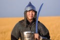 Portrait of a medieval warrior in armor with a weapon in his hands against the background of a wheat field and sky