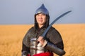 Portrait of a medieval warrior in armor with a weapon in his hands against the background of a wheat field and sky