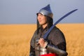 Portrait of a medieval warrior in armor with a weapon in his hands against the background of a wheat field and sky