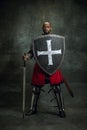 Portrait of medieval warrior, dark skinned bald knight with dirty wounded face holding shield and sword isolated over Royalty Free Stock Photo