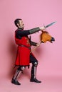 Portrait of medieval warrior or knight wearing armor clothing riding toy horse, holding big knife isolated over pink Royalty Free Stock Photo