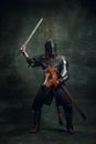 Portrait of medieval warrior or knight wearing helmet and armor riding toy horse, holding big sword  over dark Royalty Free Stock Photo