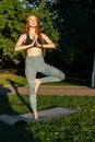 Portrait of meditative redhead young woman doing yoga in tree pose, raising hands in Namaste pose Royalty Free Stock Photo