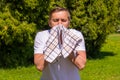 Portrait of men sneezing from allergy, in a white T-shirt, stands in the park