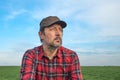 Portrait of mid-adult male farmer wearing brown cap and red plaid shirt in agricultural field, looking into distance, thinking and
