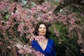 Portrait of a middle-aged brunette in a blue dress next to a cherry blossom Royalty Free Stock Photo