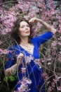 Portrait of a middle-aged brunette in a blue dress next to a cherry blossom Royalty Free Stock Photo