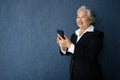 Portrait of middle aged business woman standing isolated on blue background and use smartphone for check finance, looking at the