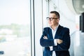 Portrait of a middle aged businessman in front of office window. Man is smiling and has his arms folded. Royalty Free Stock Photo