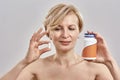 Portrait of middle aged caucasian woman holding a bottle with pills and a pill in her hands, looking at it while Royalty Free Stock Photo