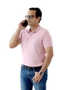 Portrait of a middle aged happy smiling Indian man in a pink T-shirt wearing glasses, standing and talking by mobile phone Royalty Free Stock Photo