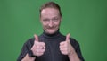 Portrait of middle-aged man with beard gesturing finger-up sign to demonstrate approvement on green background.