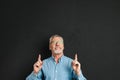 Portrait of middle aged man 50s with grey hair and beard in shirt smiling and pointing index fingers upward on copyspace, isolate Royalty Free Stock Photo