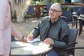 Portrait of middle-aged man sitting at table in cafe, holding pen ready to write note in notepad, looking at woman. Royalty Free Stock Photo