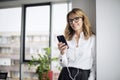 Portrait of middle aged smiling business woman using smartphone and earphone Royalty Free Stock Photo