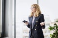 Portrait of middle aged smiling business woman using smartphone and earphones at the office Royalty Free Stock Photo