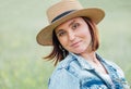 The portrait of a middle-aged smiling woman looking at the camera. She dressed in a jeans jacket, straw hat. Natural people beauty