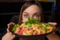 Portrait of middle-aged woman staring wide-eyed at camera, showing tasty pasta with cherry tomatoes, arugula and cheese.