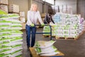 Portrait of middle aged woman working in warehouse, pushing handtruck with bags