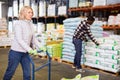 Portrait of middle aged woman working in warehouse, pushing handtruck with bags