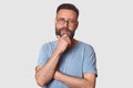 Portrait of middle bearded aged male with pensive facial expression, dressed gray cassual t shirt and round spectacles, keeps hand