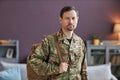 Portrait military man holding backpack and looking at camera in home setting