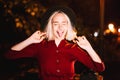 Portrait of millennial hipster woman with blond hairstyle makes funny faces, fooling around. City street at night. Hat Royalty Free Stock Photo