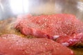 A portrait of minute beef steaks, which are thin pieces of meat. The food is cooking in a frying pan in some butter. The cow meat