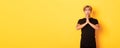 Portrait of miserable asian guy pleading, begging for help, standing over yellow background