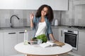 Portrait of mixed-race curly teen girl standing in the kitchen in front of a table with vegetables and a book for Royalty Free Stock Photo