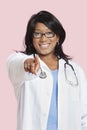 Portrait of mixed race female surgeon pointing at you over pink background