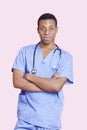 Portrait of mixed race male surgeon with arms crossed over pink background