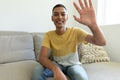 Portrait of mixed race man sitting on sofa looking at camera waving and smiling Royalty Free Stock Photo