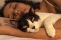 Portrait of woman with curly hair sleeping with her black and white cat in bed. Concept of love to animals, pets, care,