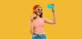 Portrait of modern cheerful laughing young woman taking selfie with mobile phone and burger fast food on yellow studio background Royalty Free Stock Photo