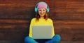 Portrait of modern happy smiling young woman working on laptop listening to music in headphones in the city park Royalty Free Stock Photo