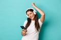 Portrait of modern pretty girl in white t-shirt, listening music in wireless headphones, holding mobile phone and Royalty Free Stock Photo