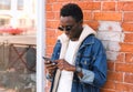 Portrait modern young african man with smartphone on city street over brick wall background Royalty Free Stock Photo