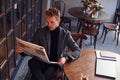 Portrait of modern young guy in formal clothes that sits in the cafe and reads newspaper Royalty Free Stock Photo