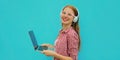 Portrait modern young woman working with laptop listening to music in headphones on blue background Royalty Free Stock Photo