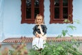 Portrait of Moldavian child girl sitting on traditional carpet against background of old windows of ancient house.