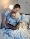 Portrait of young mother with baby boy reading book before going to sleep Royalty Free Stock Photo