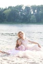 Portrait of a mother blonde and her daughter in beautiful dresses on the sand with a lake on the background. Happy family enjoying Royalty Free Stock Photo