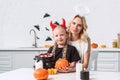 portrait of mother and daughter in halloween costumes with pumpkin at table with sweets in black pot in kitchen Royalty Free Stock Photo