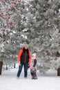 Portrait of mother and daughter standing near tree on snowy ground looking at camera smiling with rowan branches in Royalty Free Stock Photo