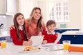 Portrait Of Mother Helping Children In School Uniform Doing Homework At Kitchen Counter Royalty Free Stock Photo