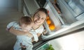 Portrait of young mother holding her baby boy and standing at open refrigerator on kitchen at night Royalty Free Stock Photo