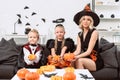 portrait of mother and kids in halloween costumes with pumpkins in hands sitting on sofa Royalty Free Stock Photo